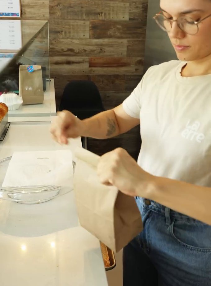 Panadera empacando un pedido de La erre en bolsa de papel